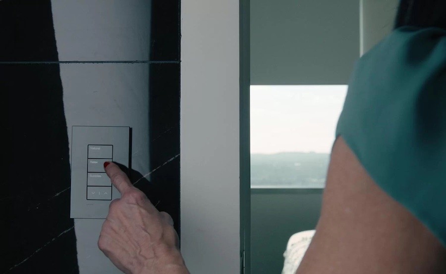 closeup of a woman’s hand tapping a button on an on-wall lighting keypad.