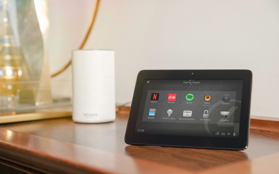An Amazon voice assistant sitting next to a touchpad featuring the Control4 home menu. 