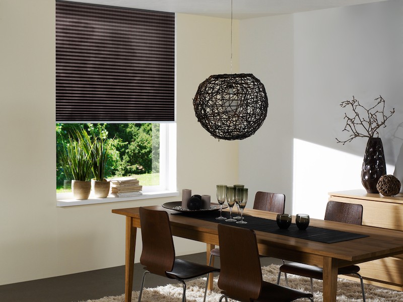 QMotion shades on a window overlooking a yard. A dining room table with four chairs sits in front of the window.